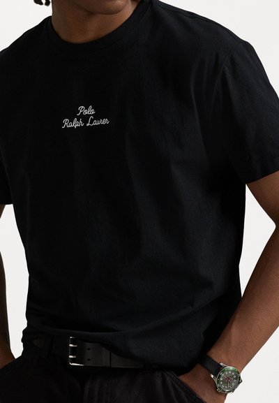 Melna kokvilnas T-kreklu ar baltu izšūtu "Polo Ralph Lauren" tekstu priekšā, īsām piedurknēm un apaļu izgriezumu.
