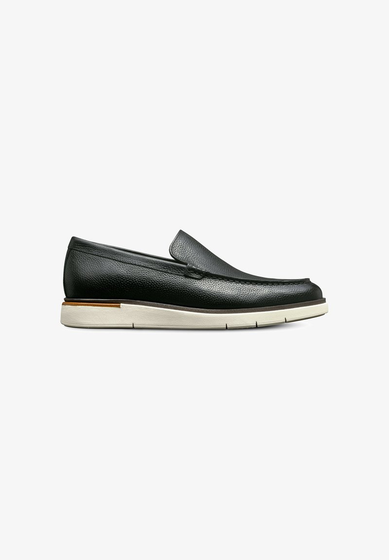 Chaussure noire en cuir à enfiler avec une surface texturée, semelle en caoutchouc crème et un petit talon. Présente un design cousu sur le devant.