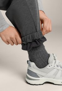 Szürke melegítőnadrág fodros fekete szegéllyel, bordázott szürke zoknival és világosszürke sportcipővel, amely texturált részleteket tartalmaz.