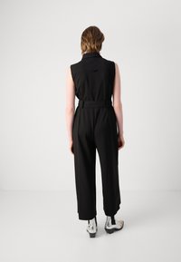 Mono sin mangas negro con cintura ceñida, diseño de pierna ancha y textura suave. Botines de tobillo plateados y negros con un diseño contrastante.