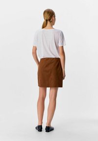 Mini gonna in suede marrone con orlo semplice, abbinata a una maglietta a maniche corte grigia chiara. Scarpe nere slip-on completano il look.