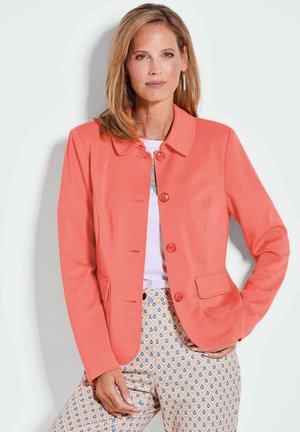Korallefarbene, weiche Jacke mit Kragen, vier Knöpfen und zwei vorderen Taschen. Kombiniert mit gemusterten Hosen mit blauen und orangefarbenen Tropfenmotiven.