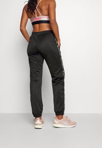 Černé sportovní kalhoty s elastickým pasem, na bocích s bílým logem. Nosené s světlou teniskou.