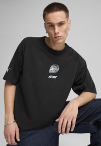 Black short-sleeve t-shirt featuring a graphic of a racing helmet and "F1" logo. Made of smooth fabric with a relaxed fit and raglan sleeves.