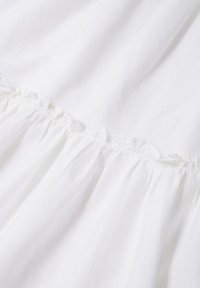 Tissu blanc avec des détails de couture froncés et volants créant une texture et des ombres subtiles sur le matériau.