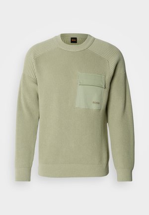 Šviesiai žalia megzta suknelė su iškilniu raštu, apvaliu kaklu ir priekinėmis kišenėmis. Kišenėje yra logotipas, o rankogaliai priglunda.