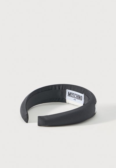 Μαύρη υφασμάτινη στεφάνη με επένδυση, με λευκή ετικέτα «MOSCHINO KID» ραμμένη στην εσωτερική πλευρά, εμφανιζόμενη σε ανοιχτό ουδέτερο φόντο.