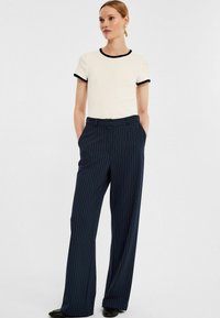 Wit top met korte mouwen en zwarte afwerking, gecombineerd met marineblauwe brede broek met streepdessin. De broek heeft zijzakken en een tailleband met een knoop.