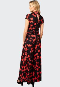 Abito maxi floreale nero con motivi di fiori rossi, maniche corte, dettaglio sul retro a chiave e vita con laccetto. Tessuto morbido con una silhouette fluente.