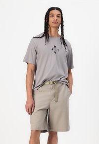 Grå bomulls t-shirt med kort ärm och svart grafisk design, parat med beige shorts med elastiskt midjeband och tygbälte.