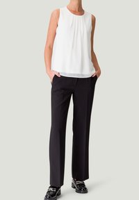 Haut sans manches blanc avec des plis, associé à un pantalon noir ajusté et long, et des chaussures noires brillantes. Texture de tissu lisse et design ajusté.