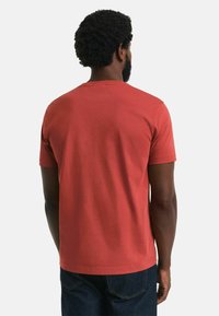 Red cotton t-shirt with a crew neck and short sleeves, featuring a smooth texture and a simple design, viewed from the back.