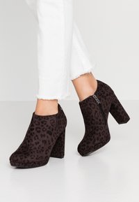 Černé kotníkové boty s leopardím vzorem, s vysokým blokovým podpatkem, polstrovanou platformou a bočním zipem. Vyrobené z materiálu připomínajícího semiš.