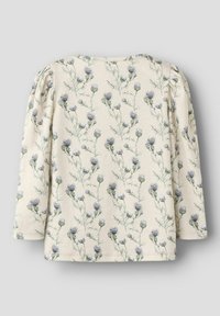 Camiseta de manga larga color crema con un patrón floral de flores de cardo púrpura y hojas verdes. Tejido suave con detalle fruncido en el hombro.