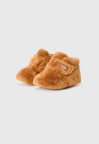 Tan, fluffy småbarnsstøvler med myk tekstur og rund form. Har en borrelåsrem og et lite, merket stoff på siden.