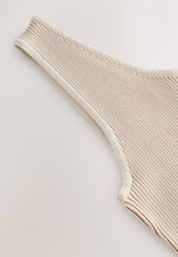 Perizoma in tessuto beige a coste con una morbida fascia elastica in vita, caratterizzato da una texture liscia e bordi cuciti puliti.