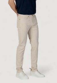 Pantalones de algodón beige con un diseño ajustado, estilo de cinco bolsillos y detalles de costura sutiles, combinados con zapatillas blancas.