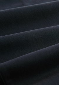 Sötétkék szövet sima textúrával, vízszintes bordákkal és hajtogatott rétegekkel, amelyek finom szín- és mélységváltozásokat mutatnak.