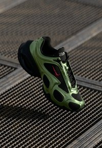 Green and black sneaker with a mesh upper, rounded sole, and textured accents; features a prominent red logo on the side.