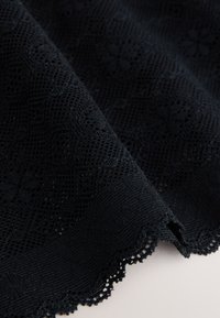 Tela de encaje negra con un patrón floral texturizado, borde festoneado y secciones de tejido abierto que crean un diseño delicado.