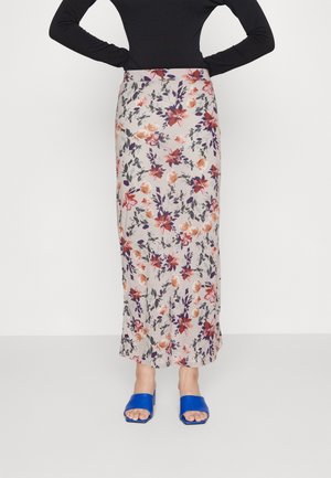 Vrouw draagt een hooggetailleerde, enkellange rok met bloemen in paars, rood en oranje, gecombineerd met blauwe open teenschoenen en een zwart topje.