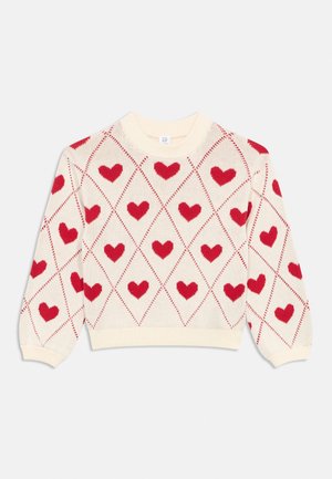 Krém pulóver hosszú ujjakkal, amely egész ruhadarabot átfogó piros szívmintával díszített rombusz alakzatokat tartalmaz.