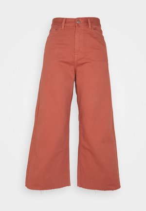 Pantalones cortos de tiro alto y pernera ancha en color terracota con cierre de botón delantero, cremallera, trabillas y dobladillo sin rematar.