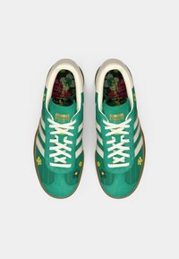 Πράσινα αθλητικά παπούτσια με σουέτ υφή, λευκές ρίγες, λουλουδάτες λεπτομέρειες και εσωτερική σόλα με σχέδιο. Διαθέτουν μπεζ λαστιχένια σόλα και κορδόνια.