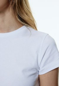 Weißes Baumwoll-T-Shirt mit rundem Ausschnitt und kurzen Ärmeln. Hat eine glatte Textur und minimale Nähte an den Ärmeln.