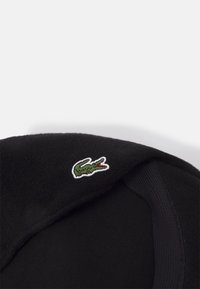 Sweatshirt noir avec un logo crocodile brodé vert et des accents rouges sur l'épaule gauche. Fabriqué en tissu doux avec des poignets côtelés.