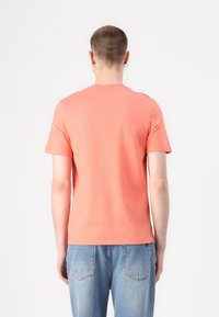 Korallfärgad bomullströja med rund hals och korta ärmar, med en slät textur och en figursydd design, tillsammans med ljusblå jeans.