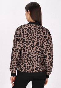 Jachetă bomber cu imprimeu leopard în nuanțe de bej cu pete negre. Dispune de un guler și manșete negre strâmte, cu o talie elastică pentru o siluetă ajustată.