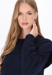 Granatowy sweter wykonany z miękkiej dzianiny, z okrągłym dekoltem i teksturowanymi bufkami, noszony przez modelkę z długimi włosami.