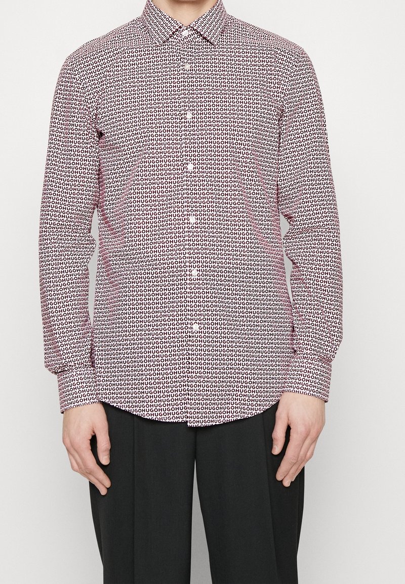 Röd- och vitrandig skjorta med långa ärmar och knappslå med upprepat textmönster. Har klassisk krage och rak fåll, gjord av lätt tyg.