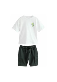 Camiseta blanca de algodón con gráfico de palmera verde y pantalones cortos tipo cargo con cordón negro, fabricados en un tejido suave y texturizado, con bolsillos laterales.