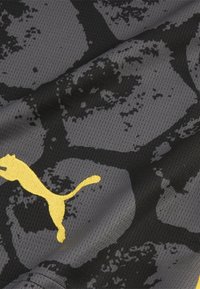 Material athletic gri cu un model abstract în nuanțe de negru și gri. Are un logo Puma galben proeminent. Textura din plasă este vizibilă pe tot parcursul.