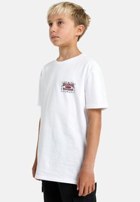 T-shirt bianco in cotone con un piccolo logo grafico colorato sulla parte sinistra del petto. Ha maniche corte e un design a vestibilità rilassata.