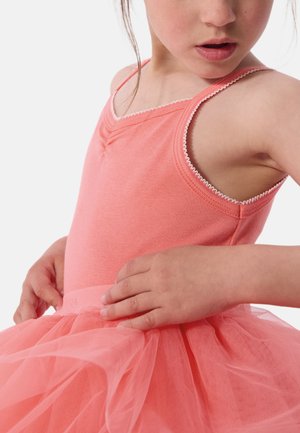 Malo dijete u ružičastoj baletnoj haljini bez rukava, prilagođava struk tila suknje s obje ruke.