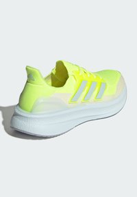 Neona dzeltena sporta apavu ar elpojošu sieta augšdaļu, atstarojošām trim svītrām, polsterētu apkakli un biezu baltu vidējo zolīti.