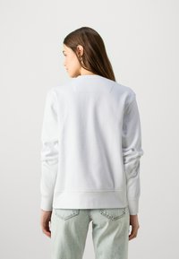 Sweat-shirt blanc en coton à manches longues, col rond et un détail en yoke rectangulaire au dos, associé à un jean bleu clair.
