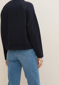 Marinblå kortad sweatshirt med strukturerad tyg, sänkta axlar och avslappnad passform. Kombinerad med ljusblå jeans med vanliga bakfickor.