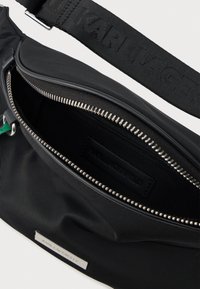 Černá nylonová crossbody taška s kovovým zipem, vnitřní kapsou a značkovou nášivkou. Obsahuje texturovaný nastavitelný popruh.