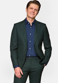 Ciemnozielony garnitur o teksturowanym wykończeniu, w połączeniu z jednolitą granatową koszulą. Posiada dwa guziki, wyłogi w kształcie notcha oraz smukły fason.