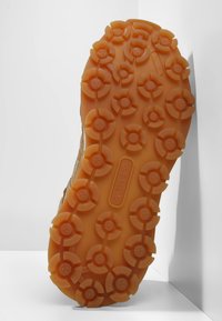 Ruskea kuminen kengänpohja, jossa on pyöreitä pintakuvioita ja voimakkaita pito yksityiskohtia. "Adidas" -logo kaiverrettuna välipohjaan.