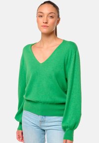 Pull green tricoté avec un col en V, des manches ballons et un ourlet côtelé. Fabriqué dans un matériau doux et possède une coupe décontractée. Associé à un jean bleu clair.
