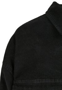 Schwarze Cordjacke an Schulter und oberem Rücken mit sichtbarer Rippenstruktur und Kragen-Detail auf weißem Hintergrund.