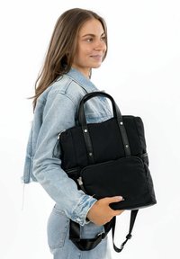 Mochila de tela negra con asas dobles, bolsillo frontal con cremallera y correa de hombro ajustable. Presenta una textura suave y detalles en metal plateado.