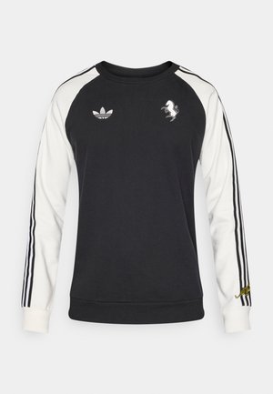 Juodas džemperis su baltais raglano rankovėmis, kuriose yra trys juodos juostelės, išsiuvinėtais logotipais ir minkšta tekstūra. Klasikinio stiliaus apvalios iškirptės dizainas.