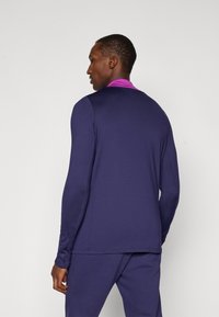 Navy long-sleeve shirt with a pink collar. Smooth fabric, fitted design, and seamless shoulders. Matched with navy pants, viewed from the back.