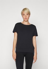 T-shirt nera a maniche corte con vestibilità rilassata e scollatura rotonda, caratterizzata da una texture morbida e un orlo leggermente più lungo in vita.